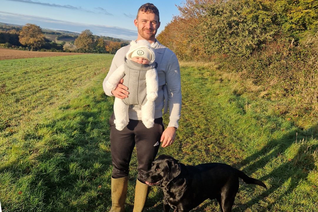 Photo shows walking for charity app trundl member Liam walking outdoors with his baby daughter and dog.