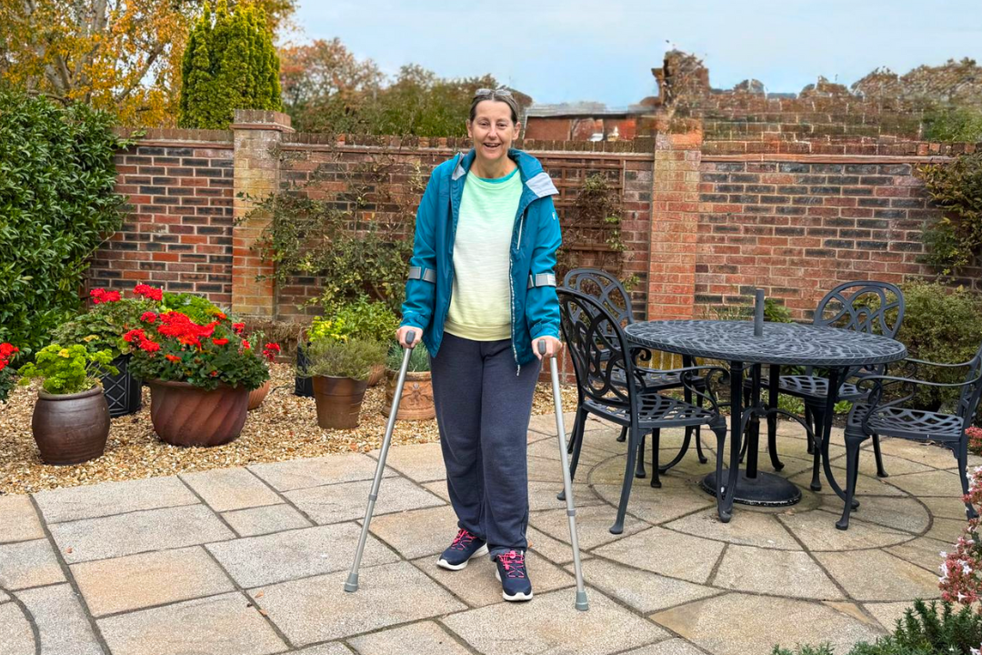 Founder of walking for charity app trundl stands in a garden resting on 2 crutches after her 2nd hip operation