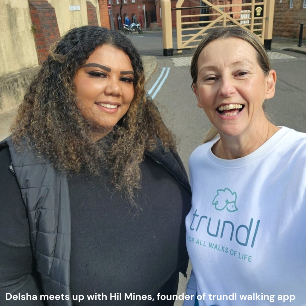 Two women stand together smiling, one wears a t-shirt showing trundl the walking for charity app